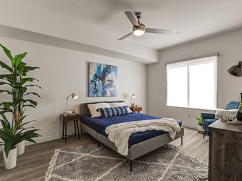 A bedroom with a bed, a ceiling fan, and a painting on the wall.